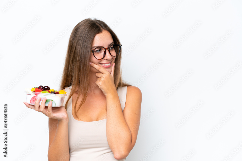 Young pretty woman holding a bowl of fruit isolated on white background thinking an idea and looking side Young pretty woman holding a bowl of fruit isolated on white background thinking an idea and looking side
