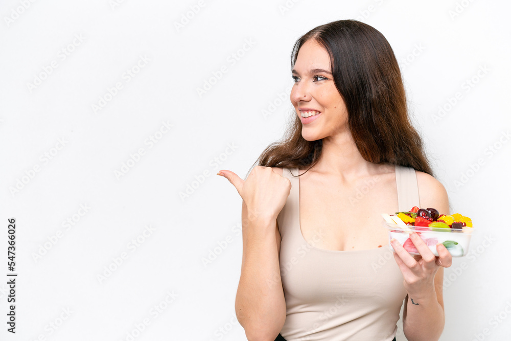 Young caucasian woman holding a bowl of fruit isolated on white background pointing to the side to present a product Young caucasian woman holding a bowl of fruit isolated on white background pointing to the side to present a product