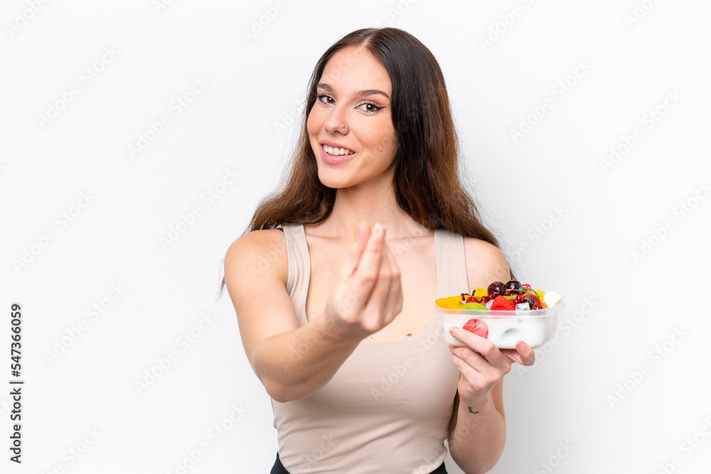 Young caucasian woman holding a bowl of fruit isolated on white background making money gesture