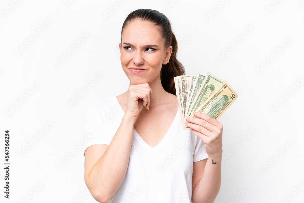 Young caucasian woman taking a lot of money isolated on white background having doubts and thinking Young caucasian woman taking a lot of money isolated on white background having doubts and thinking