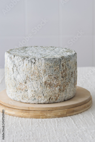 Whole round blue cheese wheel on wooden cutting board on light background, selective focus