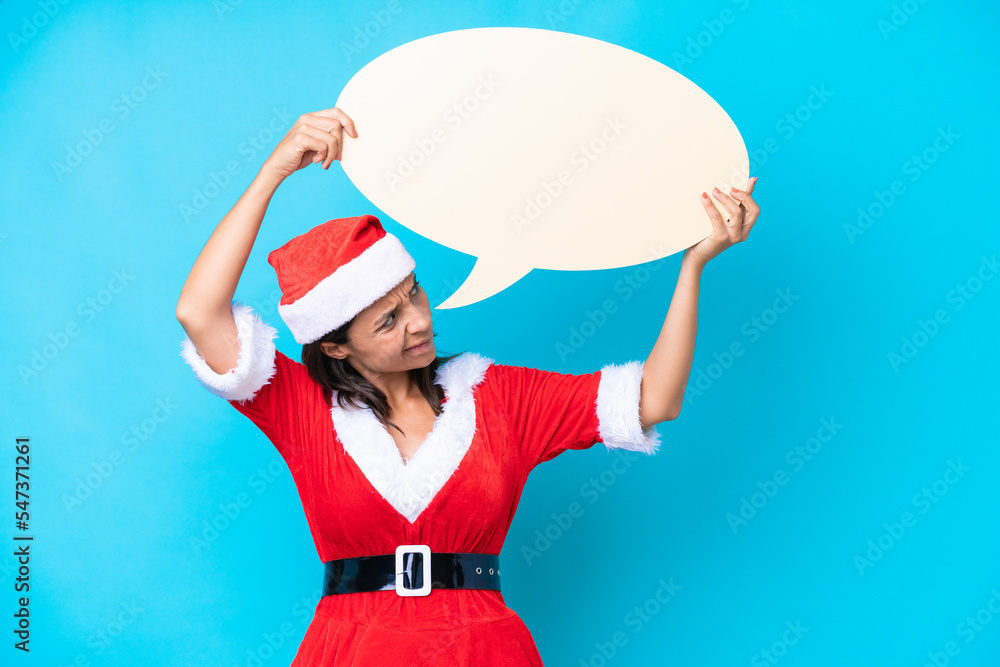 Obraz premium Young hispanic woman dressed as mama noel isolated on blue background holding an empty speech bubble and with sad expression