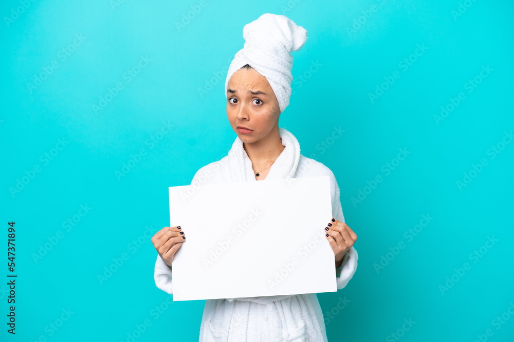 Young woman in a bathrobe with towel isolated on blue background holding an empty placard Young woman in a bathrobe with towel isolated on blue background holding an empty placard