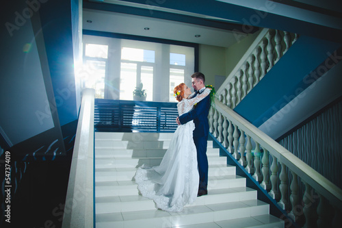 Young beautiful couple in a blue suit and white wedding dress with a bouquet in the hotel