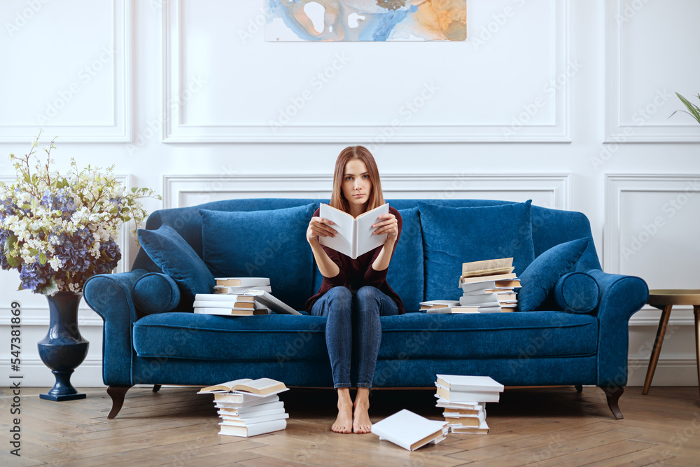 Young bored woman with a book on a spacious sofa in the living room.
