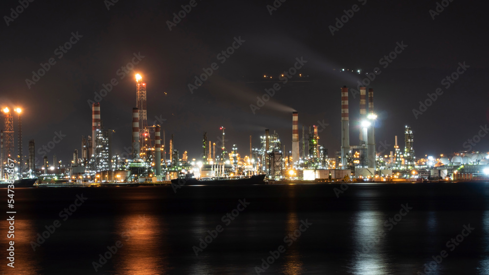 Oil refinery plant at night. Long exposure of factory lights reflection on sea. Noise and grain included.