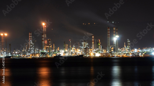 Oil refinery plant at night. Long exposure of factory lights reflection on sea. Noise and grain included.