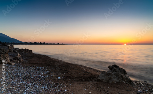 peaceful sunset over the ocean with silhouette of mountains and pebble beach iwth rock boulders in the foreground