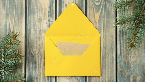 Stop motion video of bright yellow opening envelope on gray wooden background with branches of Christmas tree. Kraft paper card is taken out of new year envelope and opened. Copy space. Top view