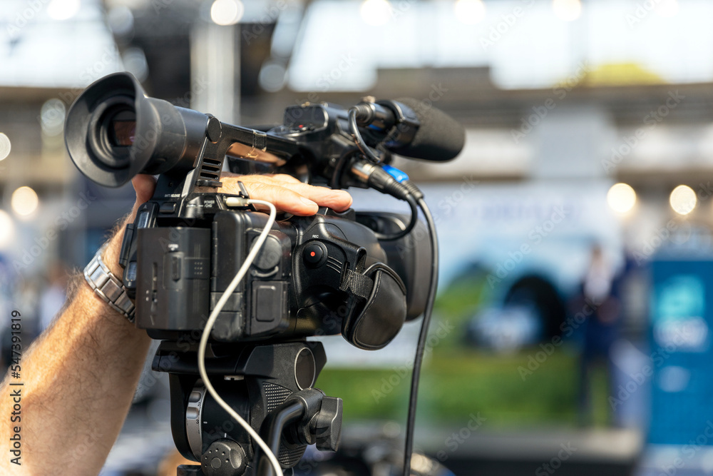 Camera operator filming media event, news or press conference with a professional video camera