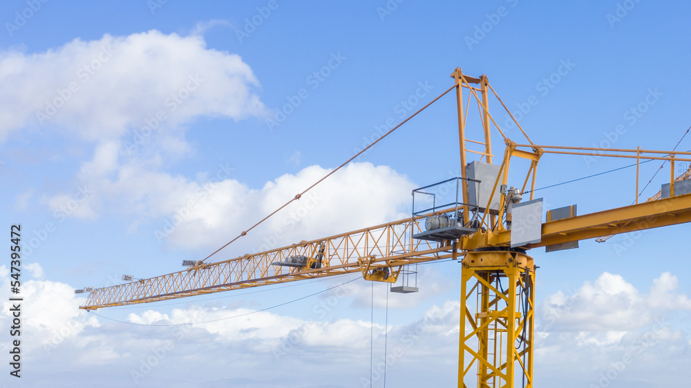 Aerial view of a yellow industrial tower crane operating in high building construction site. These large machines allow the concrete plates weight balance. City development concept.