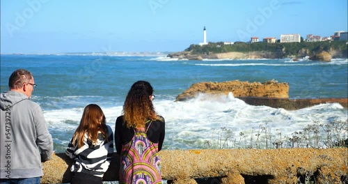 Mom and her daughter watching the swell breaking on the beach of Biarritz with its famous lighthouse on the horizon