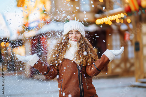 Happy smiling woman catching snowflakes, posing at festive street market. Festive Christmas fair, winter holidays concept.