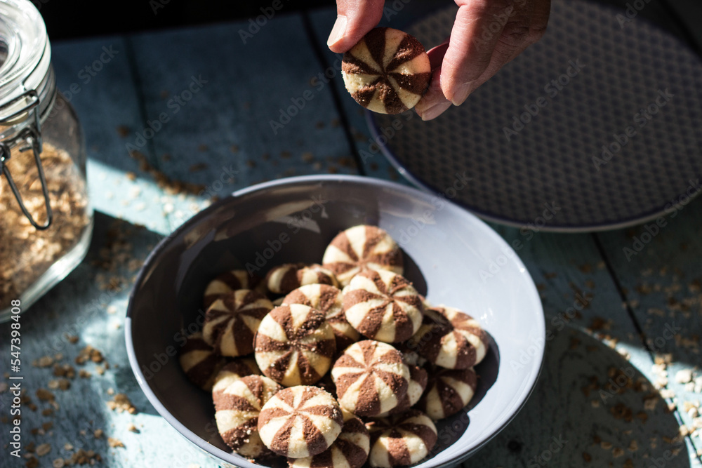 Sweet chocolate cookies on rustic wooden table with flakes. Woman hand holding cookies