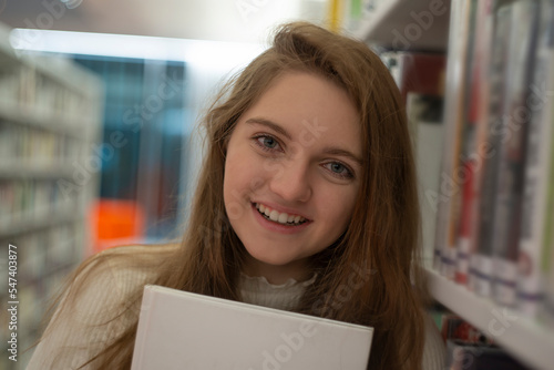 Portrait of happy beautiful young student. She is reading in modern university library.
