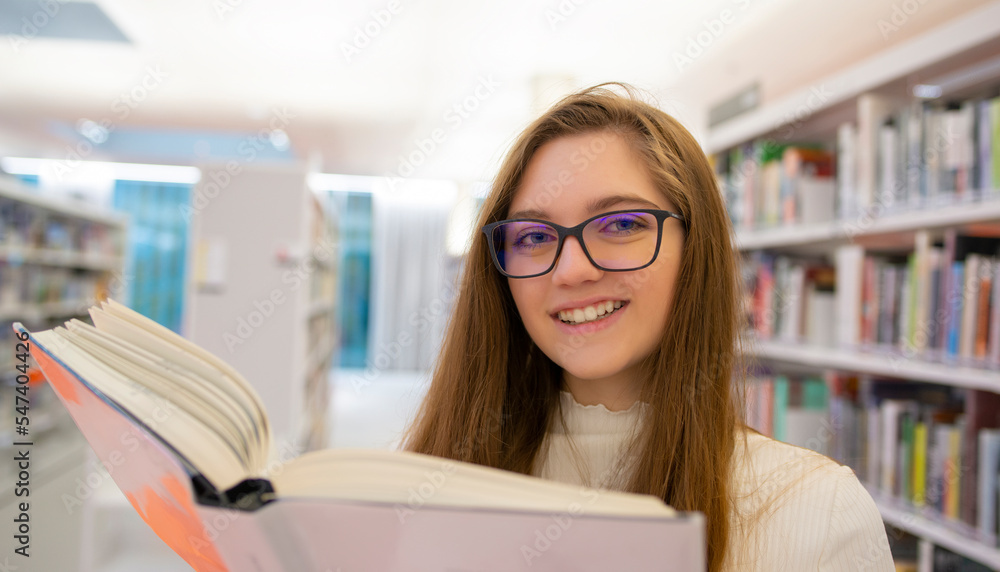 Portrait of happy beautiful young girl in eyeglasses. Happy student is reading in modern university library. Portrait of happy beautiful young girl in eyeglasses. Happy student is reading in modern university library.