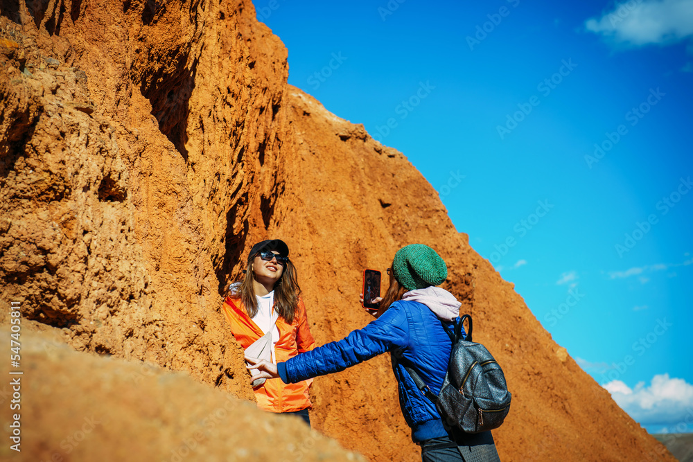 Woman tourist photographing her girlfriend on red canyon background. Female hipsters traveling in mountains. Woman tourist photographing her girlfriend on red canyon background. Female hipsters traveling in mountains.