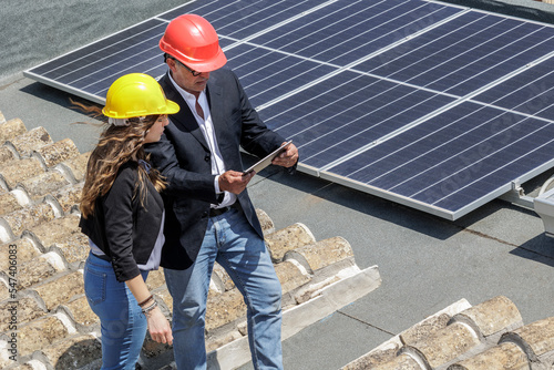 Coppia Coppia di Ingegneri con caschetto protettivo verifica lo stato di un  impianto fotovoltaico sul tetto di una casa utilizzando un tabletdi Ingegneri impianto fotovoltaico photo