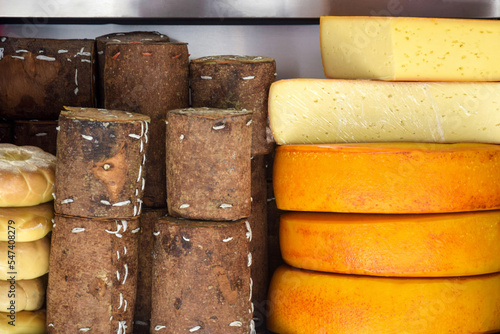 Cheese heads of different colors and sizes are stacked on counter. Fair trade in homemade cheese. Close-up. Selective focus. photo