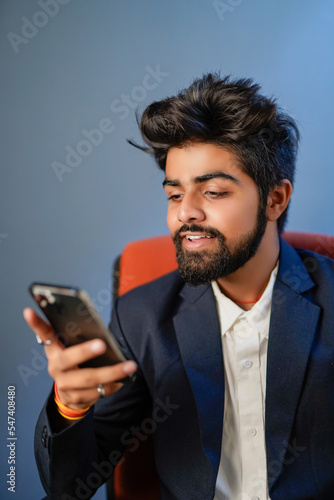 Businessman sitting on chair isolated. Handsome young indian businessman using mobile phone, confident smile looks. half shot.