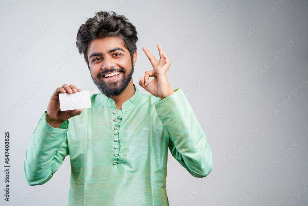Fototapeta premium Young indian man wearing traditional and showing card on white background