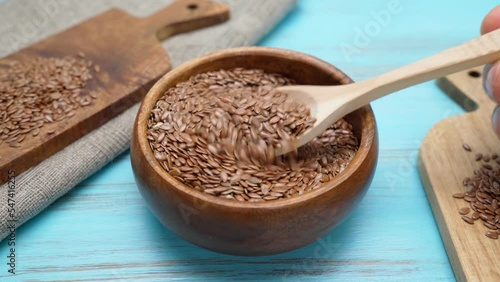 Flax seed flaxseed pouring from wooden spoon scoop into wooden bowl.