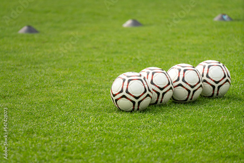 Soccer balls on firm grass ground which are prepared for the training session. Sport equipment object photo  selective focus.