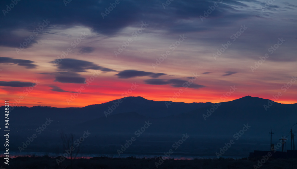 Very early scenic dawn with red, orange and blue sky colors with mountain views on the horizon.