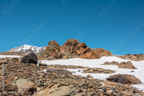 Scenic mountain landscape with old rocks and stones among snow in sunlight. Awesome alpine scenery with stone outliers on high mountain under blue sky in sunny day. Sharp rocks at very high altitude.
