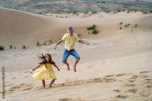Children jump on sand dunes through sand dust driven by wind on summer holidays