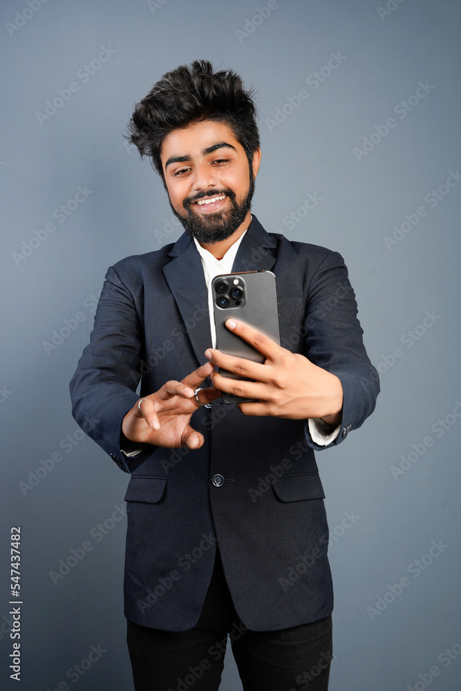 Portrait of a handsome happy young businessman wearing suit standing isolated over gray background, using mobile phone, video call concept Portrait of a handsome happy young businessman wearing suit standing isolated over gray background, using mobile phone, video call concept
