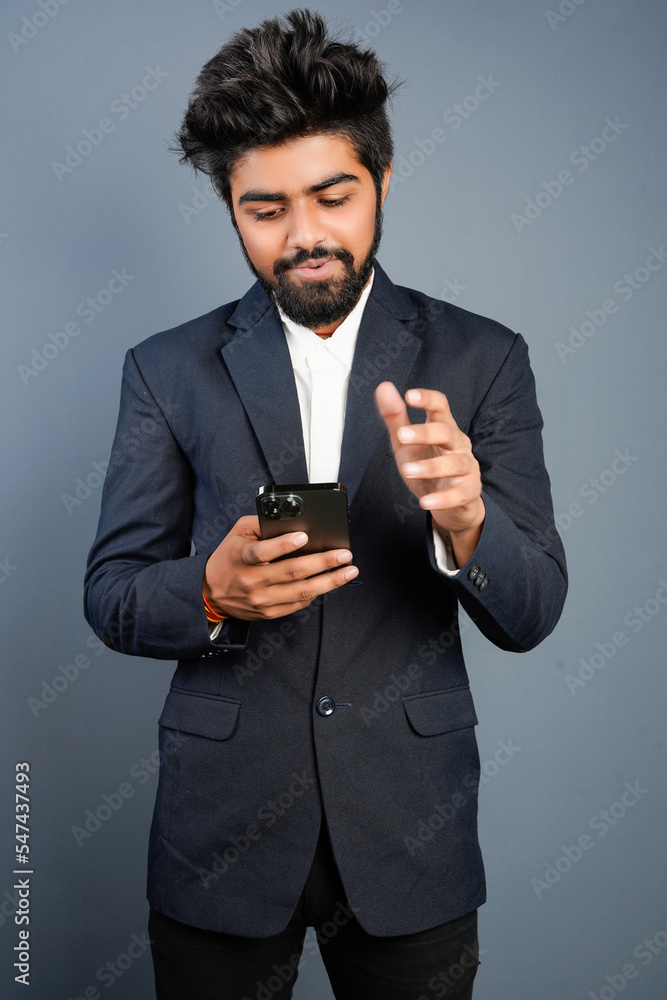 Portrait of a handsome happy young businessman wearing suit standing isolated over gray background, using mobile phone, video call concept Portrait of a handsome happy young businessman wearing suit standing isolated over gray background, using mobile phone, video call concept