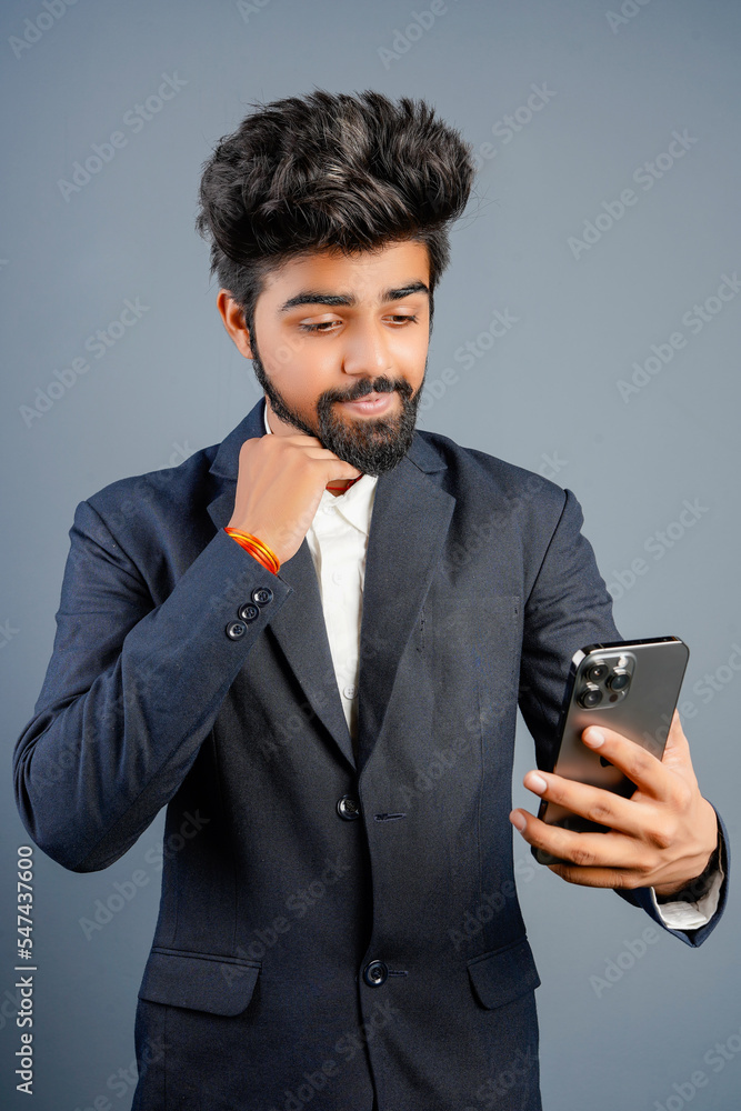 Portrait of a handsome happy young businessman wearing suit standing isolated over gray background, using mobile phone, video call concept Portrait of a handsome happy young businessman wearing suit standing isolated over gray background, using mobile phone, video call concept