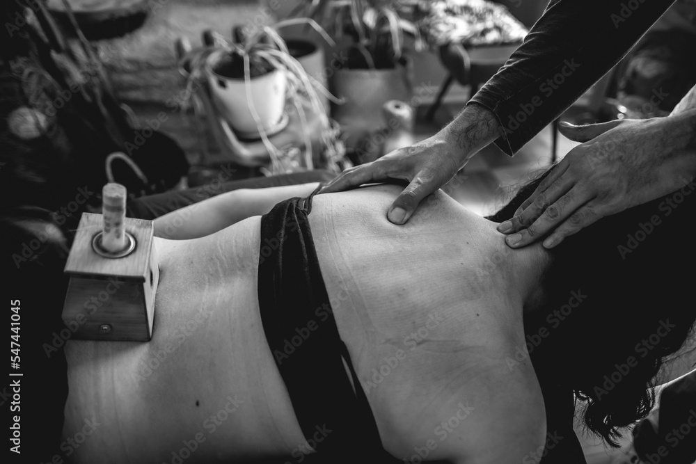 Obraz premium Traditional chinese medicine doctor in the consult doing a massage to a teenager girl patient with herbal moxa stick in a smoke box in the back (moxibustion) (in black and white)