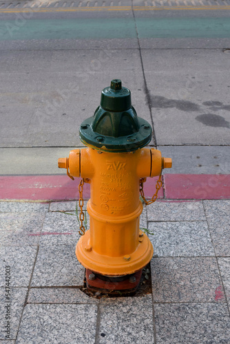 Bright yellow fire hydrant valve on a street with multi-colored stripes