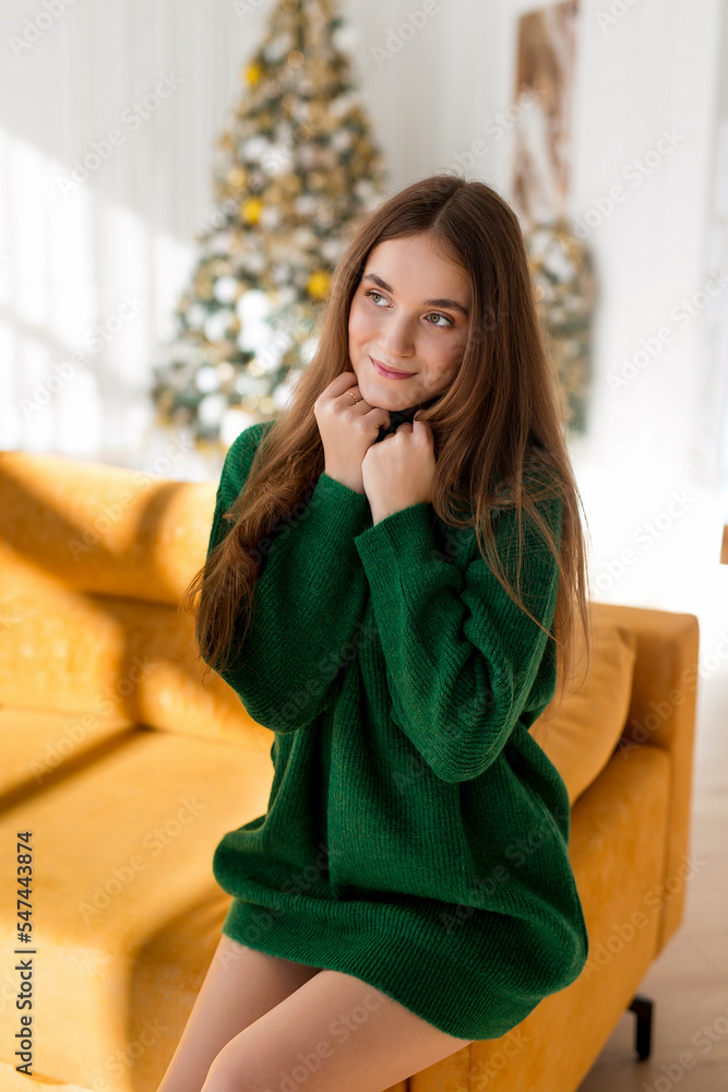 Happy young and beautiful woman celebrating Christmas. Girl in green sweater posing against the background of the Christmas tree.