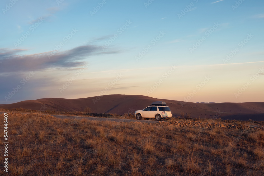 White car suv parked near scenic route road in autumn Caucasus landscape. Natural Caucasus landmark and popular destinations. Luggage trunk box mountained on car roof rack. White car suv parked near scenic route road in autumn Caucasus landscape. Natural Caucasus landmark and popular destinations. Luggage trunk box mountained on car roof rack.