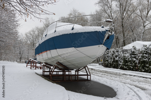 The motorboat is covered with a cover and stands outdoors in the snow. Preparing the boat for winter