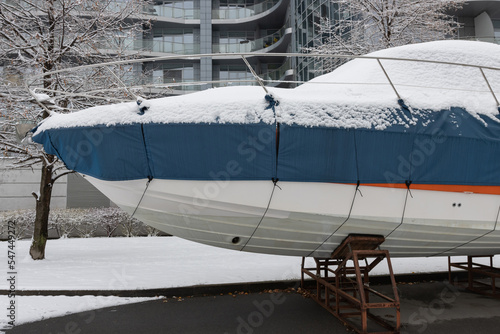 The motorboat is covered with a cover and stands outdoors in the snow. Preparing the boat for winter
