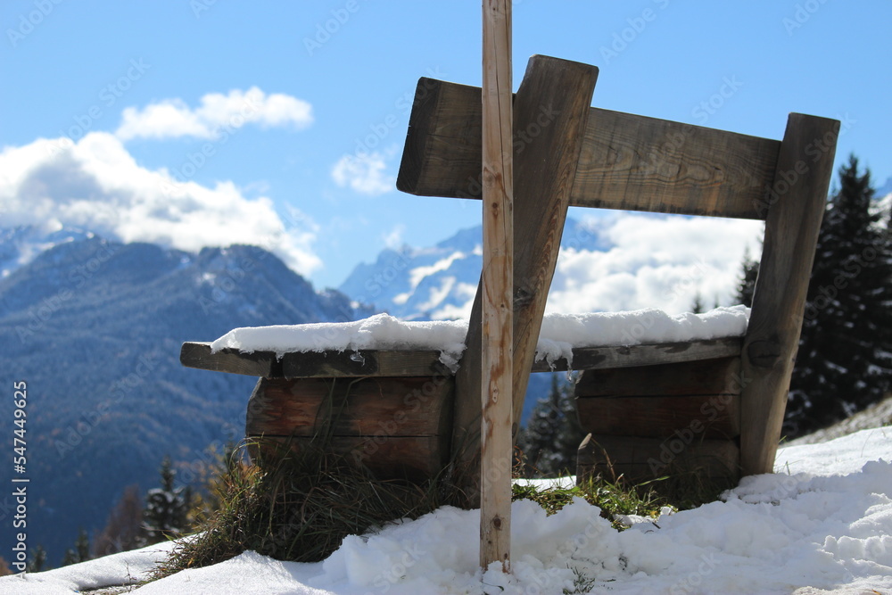 Snow covered bench with a wooden pole in front at a mountain lookout point in winter. Concept for winter thoughts, resting in winter, Switzerland, winter background or wallpaper, taking in the view