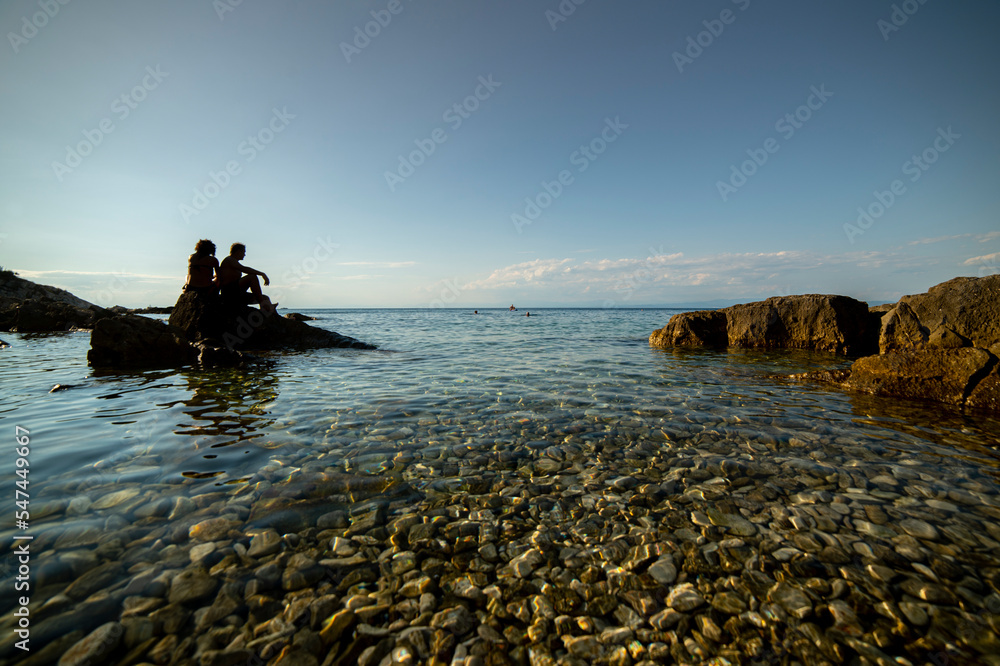 A couple in love is sitting on the rocks in the sea, relaxing and enjoying