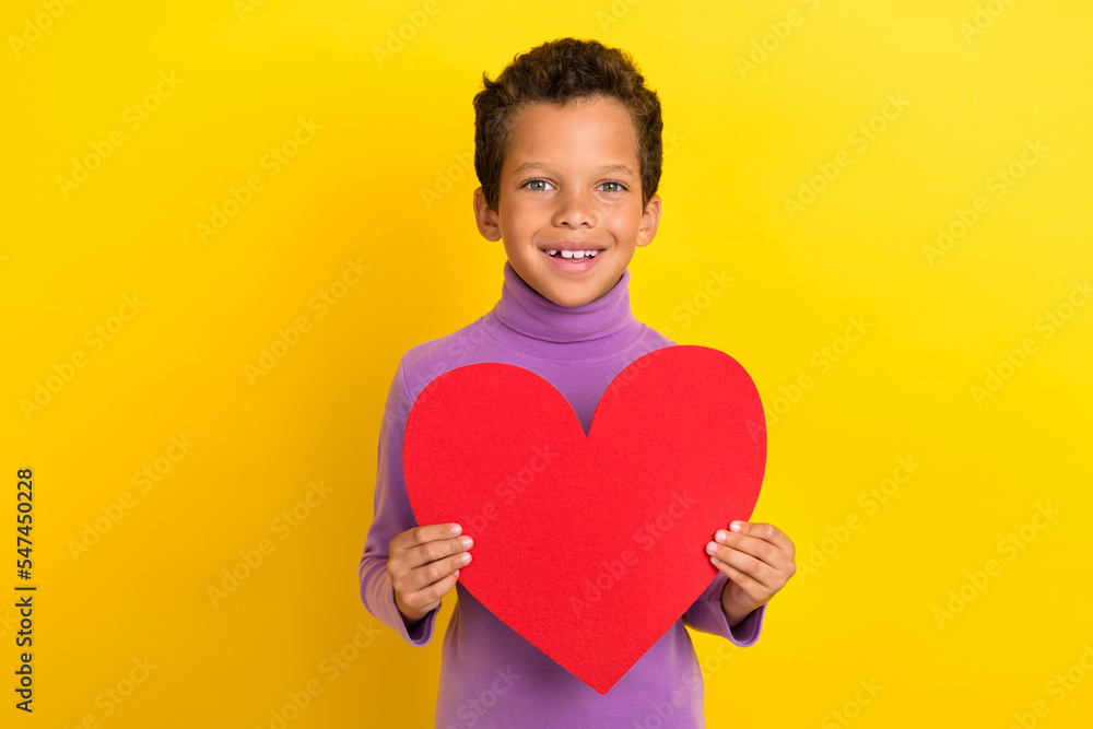 Photo portrait of charming little pupil boy hold large red heart paper shape wear trendy violet clothes isolated on yellow color background Photo portrait of charming little pupil boy hold large red heart paper shape wear trendy violet clothes isolated on yellow color background
