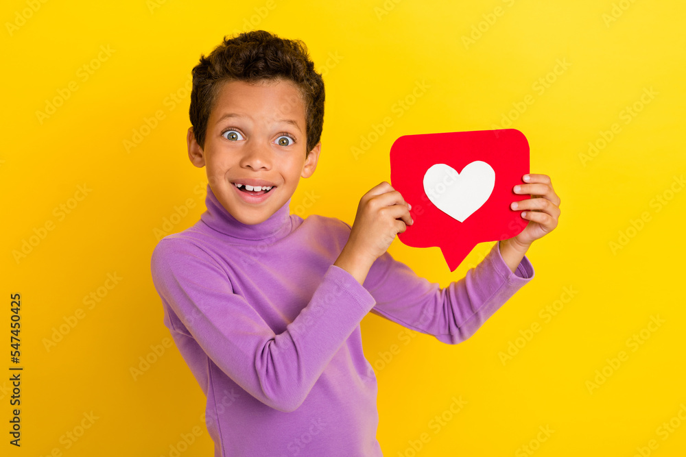 Portrait of funny astonished boy arms hold paper like card beaming smile isolated on yellow color background