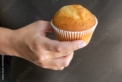 Female hand with tasty cupcake on the brown background, junk food concept