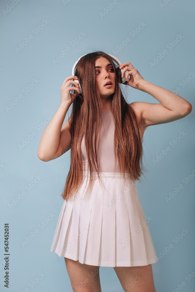 A girl with long hair listens to music with white headphones on a blue background. 