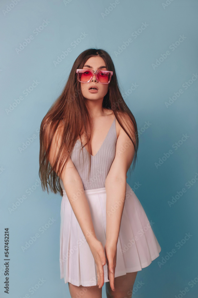 A girl with long hair with makeup and pink glasses in the style of a Barbie doll on a blue background.
