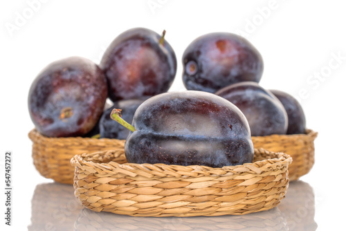 Several organic plums in straw plates, close-up, isolated on a white background.