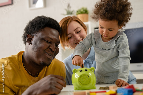 A child is putting a coin into a piggy- bank. Savings bank accounts for kids concept. Child saving money for future - concepts. Multi-ethnic  family