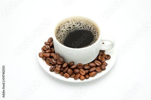 A cup of coffee with a beautiful foam stands on a saucer with coffee beans scattered on it. Isolated on a white background