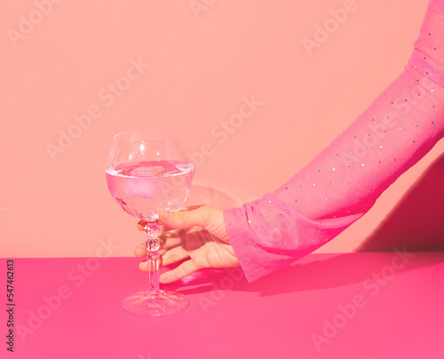 Pink gin cocktail in a highball glass and female hand against bright wall. Girls party idea. 